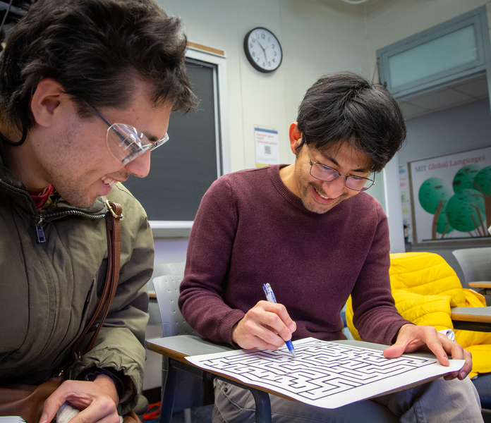 Two students seated at desks review a line-drawing maze. Both are wearing safety glasses.