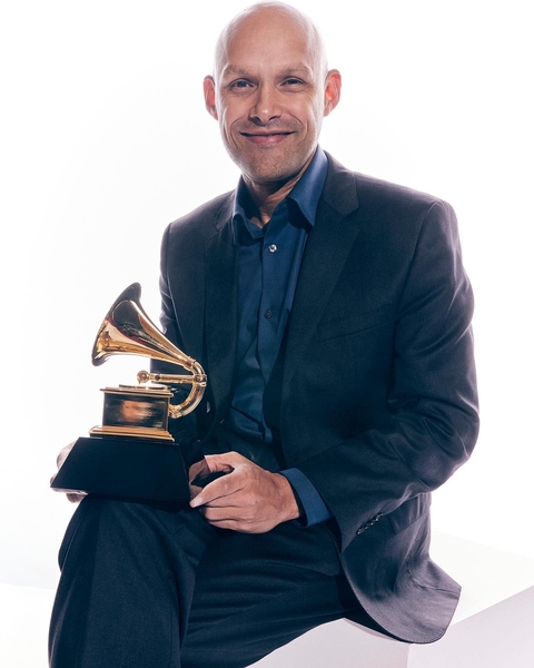 Miguel Zenón, seated, poses with his Grammy Award against a white background