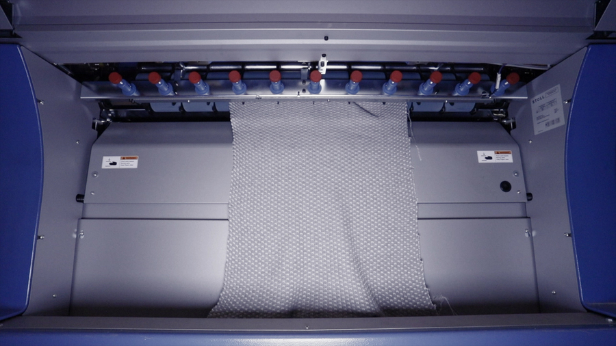 Closeup of the interior of a knitting machine with grey textile material inside