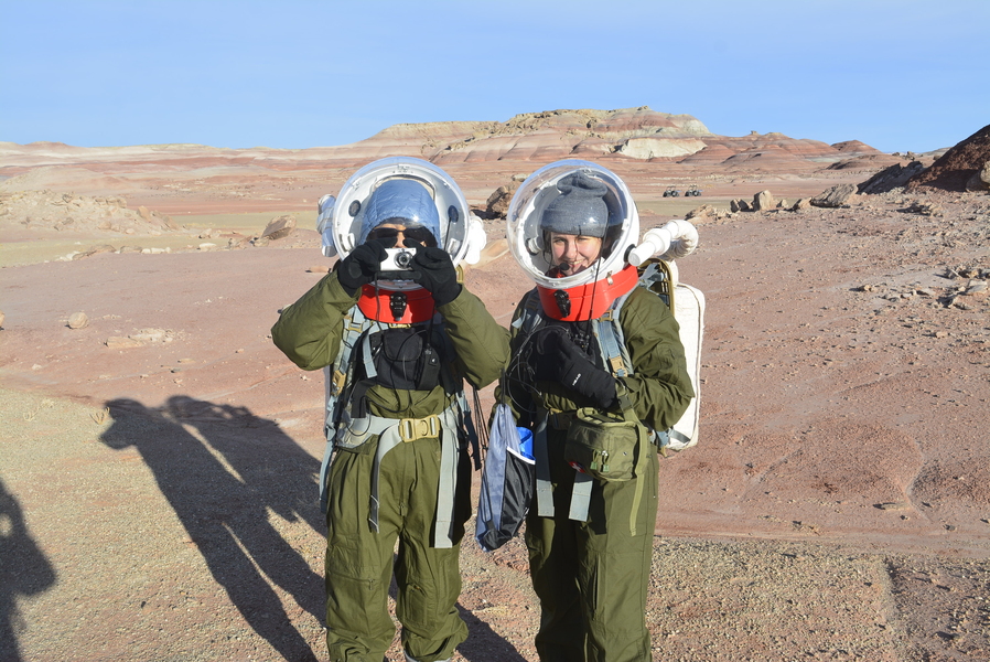 Madelyn Hoying and Wing Lam Chan pose in EVA suits, Chan taking a photo with a small camera.