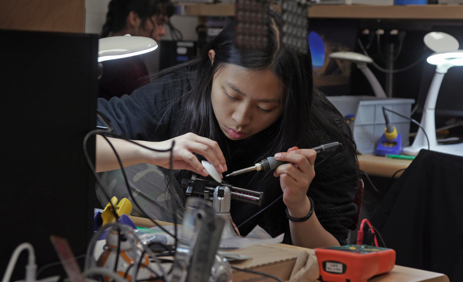 Seated at a lab table, Audrey Chen solders a circuit board