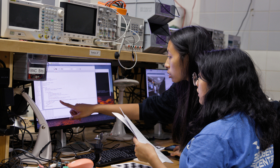 Audrey Chen and Jessica Lam sit in front of a computer screen, pointing at lines of code