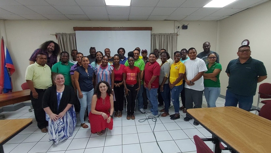 About 28 people pose together in a room with a wood table and a projector screen