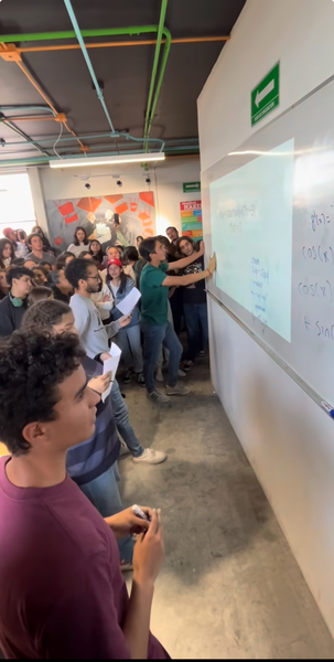 Side view of a group of students standing in front of a whiteboard while spectators look on.