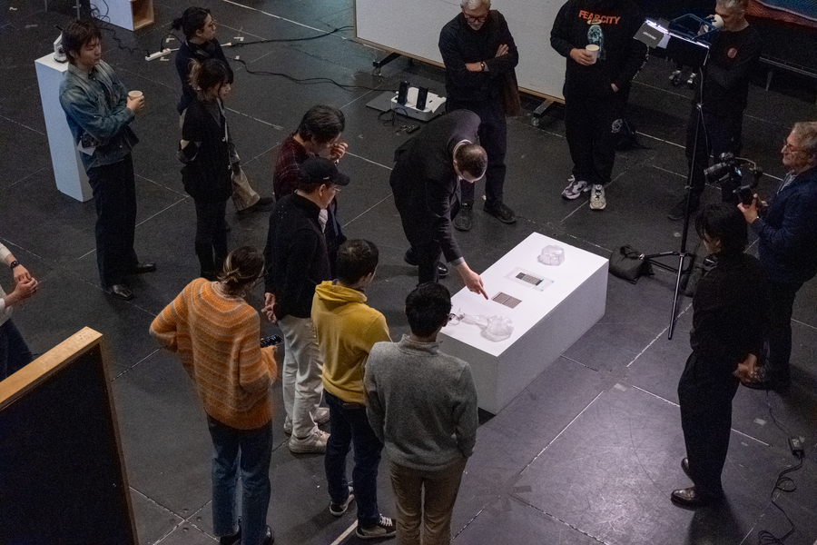 Image shot from above of about a dozen students and faculty looking at artwork presented on a white box