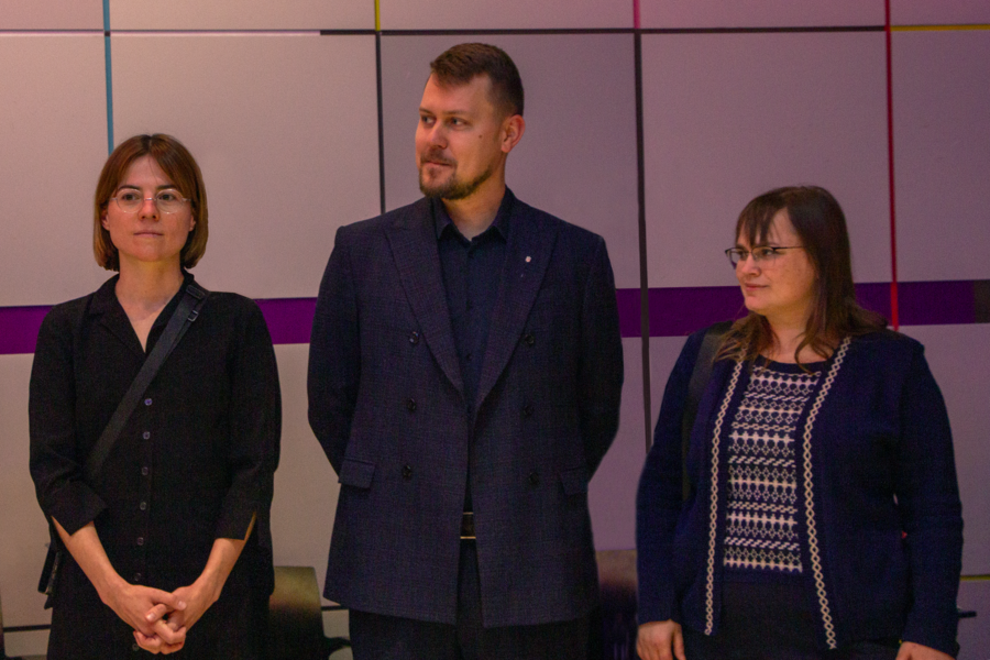 Kateryna Lopatiuk, Dmytro Chumachenko, and Liudmyla Huliaieva stand together in front of a white tiled wall