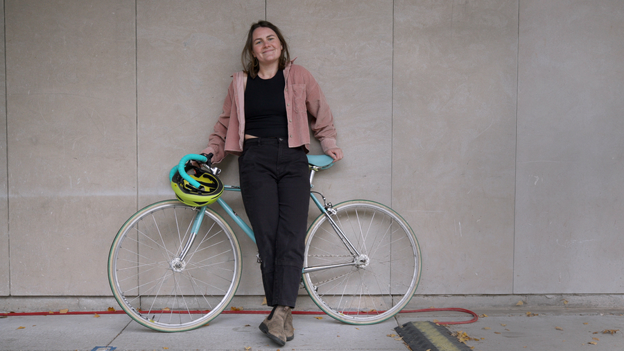 Bianca Champenois poses against a concrete wall with her bicycle 