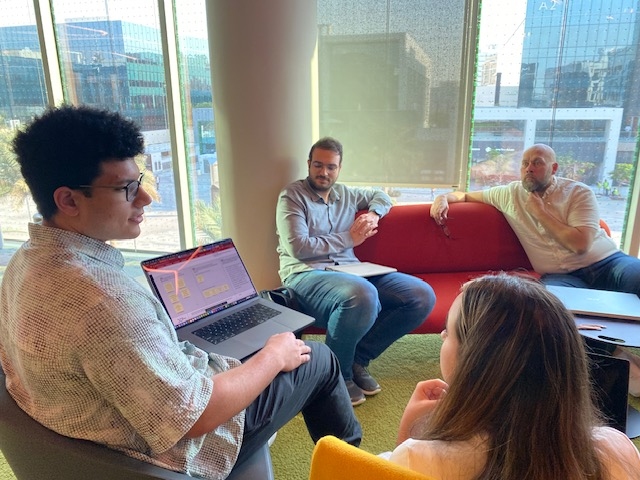 Four people sitting around, discussing something on a shared laptop