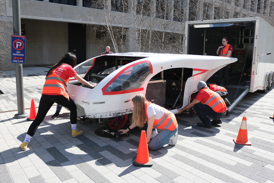 Students crouch around large white solar vehicle as they pull it from their trailer