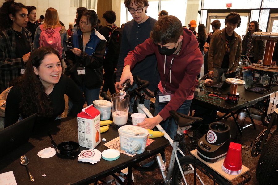 Students smile amongst a crowd as they scoop ice cream into a bike-powered blender