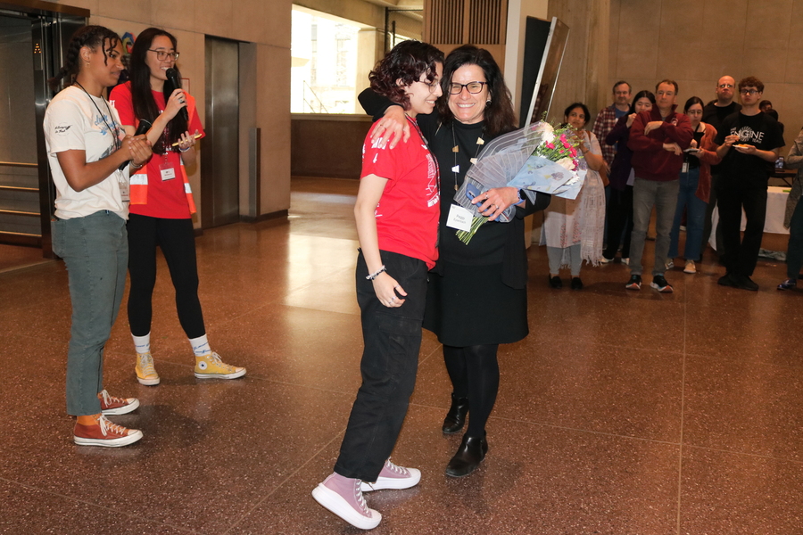 Peggy Eysenbach, holding flowers, hugs a student as others clap