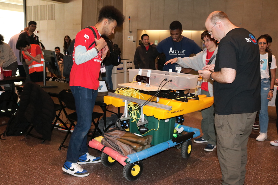 Visitors look at bright yellow autonomous boat sitting on a wheeled cart