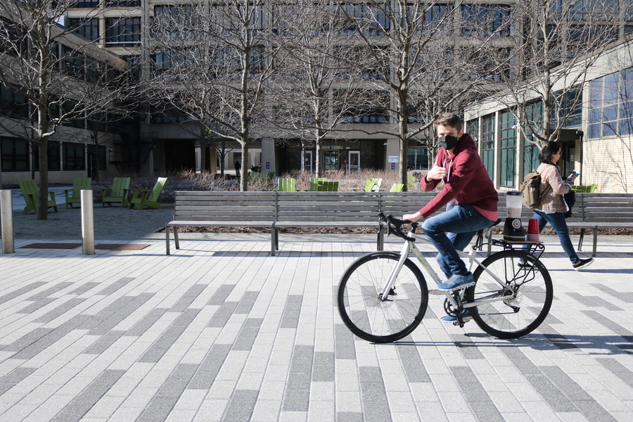 Student gives thumbs up as he rides a bike down the outfitinite with a blender on the back