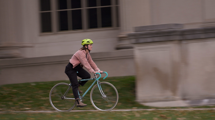 Bianca Champenois rides a bike in front of a marble building on the MIT campus.