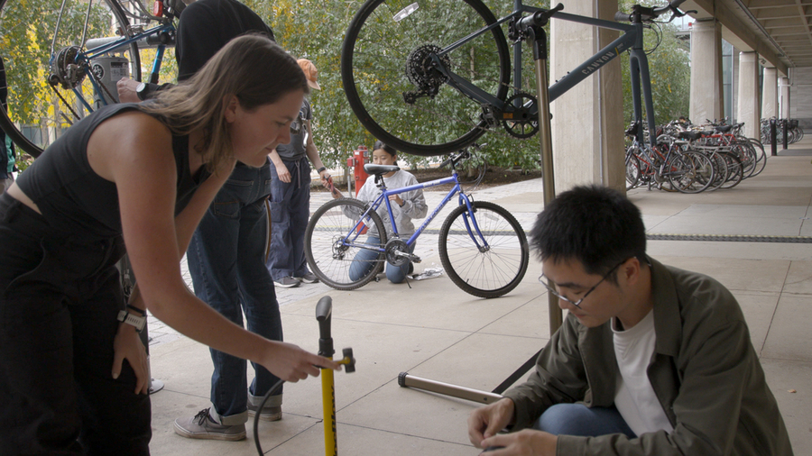 Two students bend over a bicycle, conducting maintenance.
