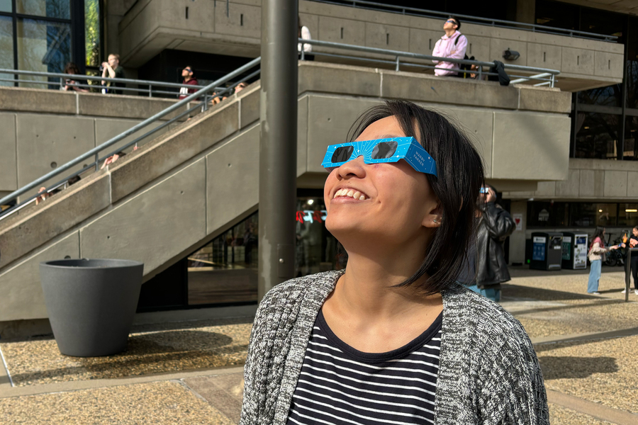 Joanna Chen wears special eclipse glasses and look up, with other people doing the same in background.