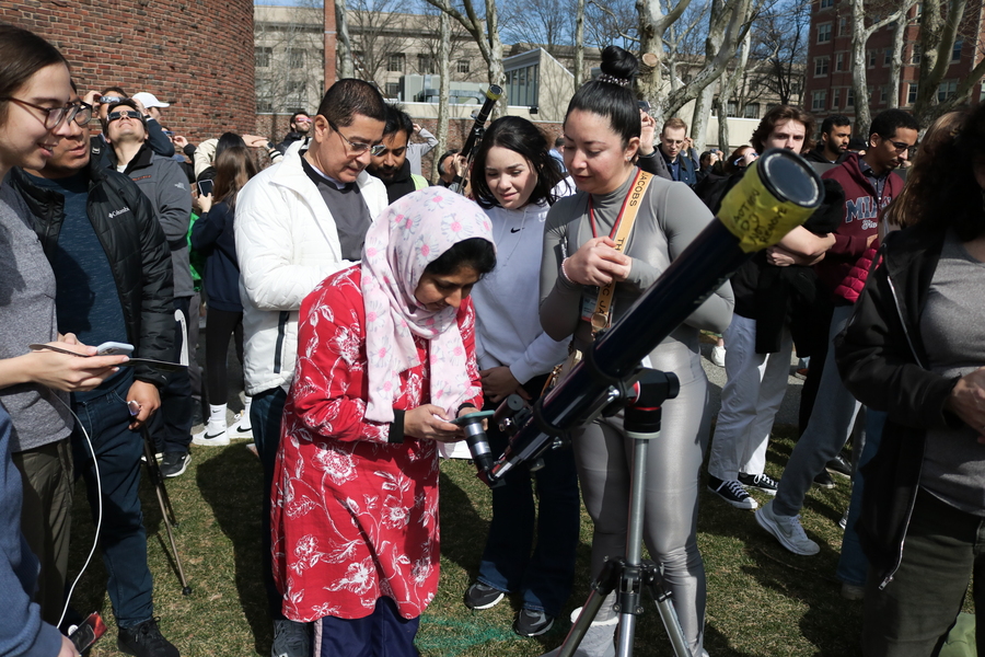 A woman takes a photo through a large telescope, as a crowd watches.
