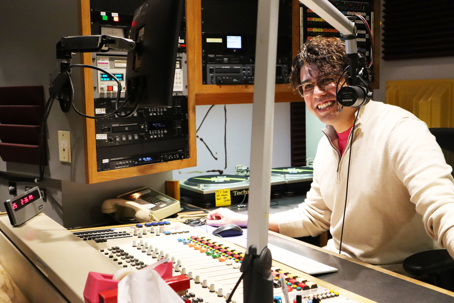 Matthew Roman sits at a control board, smiling