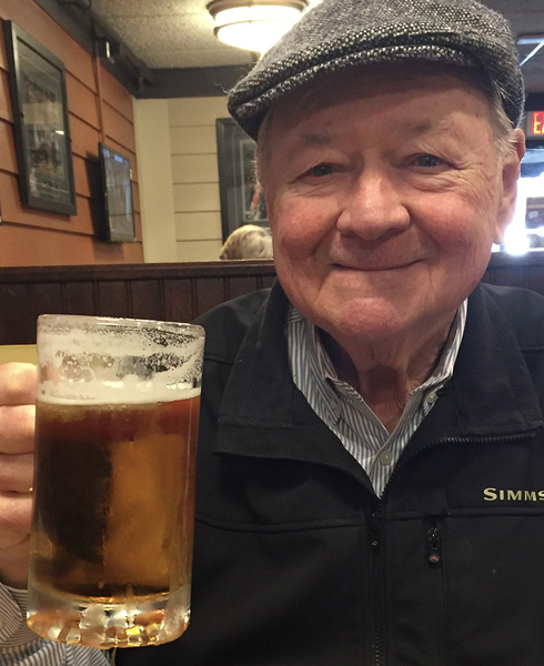 Closeup of Bernie Wuensch smiling in a restaurant, holding a glass mug filled with beer
