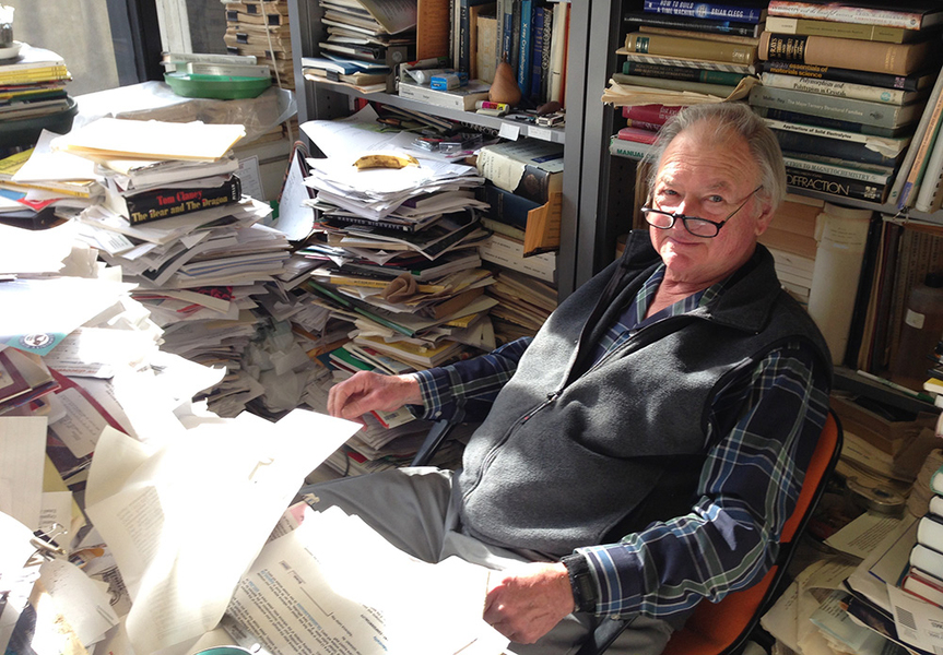 Photo of Professor Emeritus Bernie Wuensch sitting in his office, with books and stacks of paper all around him.