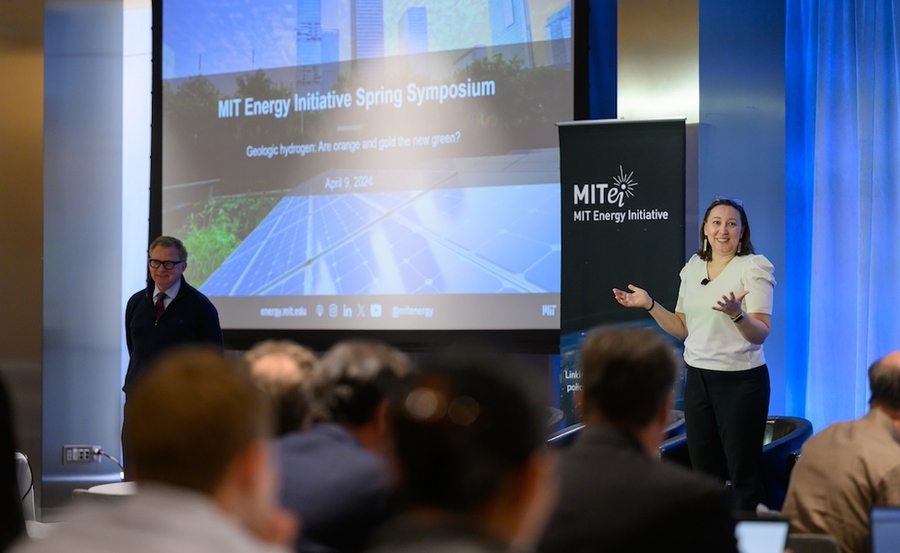 Mary Haas stands on stage addressing audience. Moderator stands on the left side of the stage