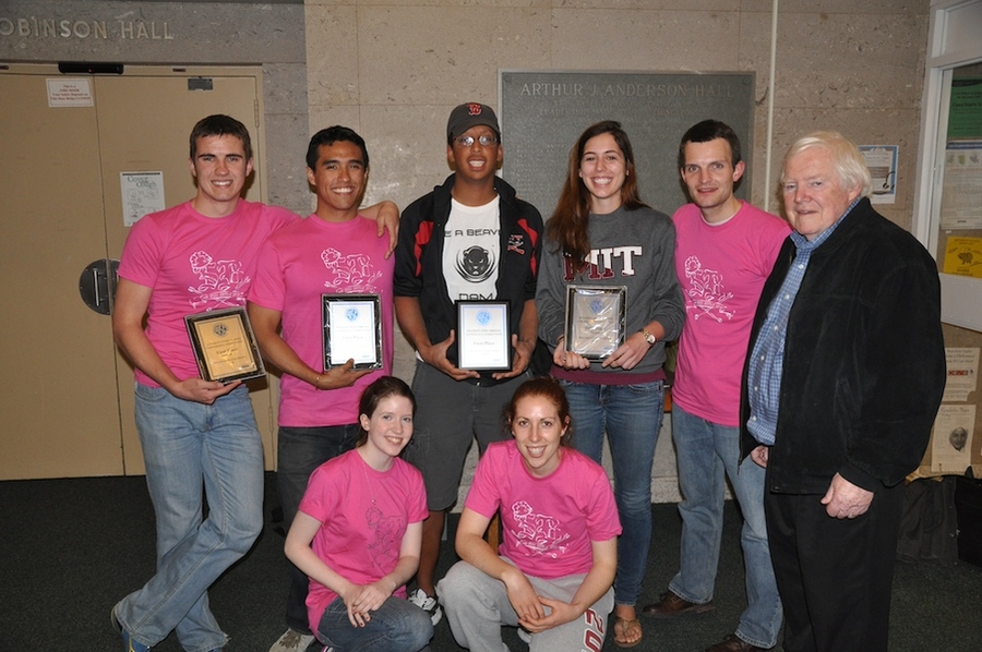 Photo of 7 students, 5 of them wearing pink team T-shirts, holding plaques with Jerome Connor