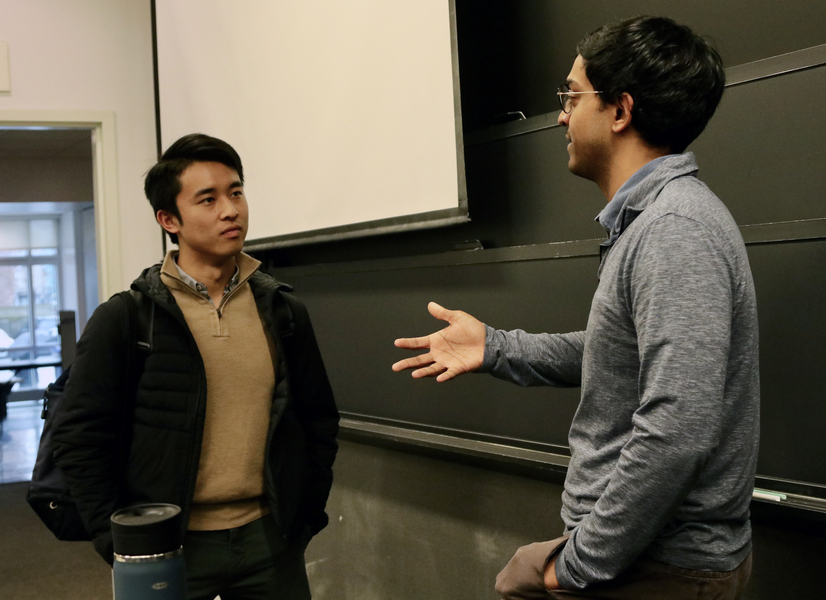 Ashesh Rambachan converses with a student in the front of a classroom.
