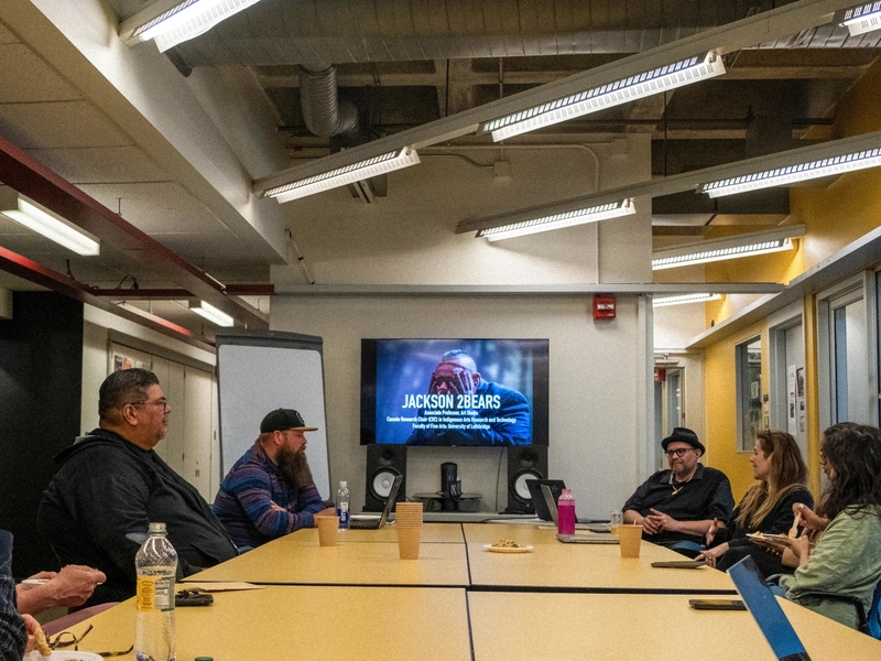 Six people sit around a large conference table in front of a screen that says "Jackson 2bears"