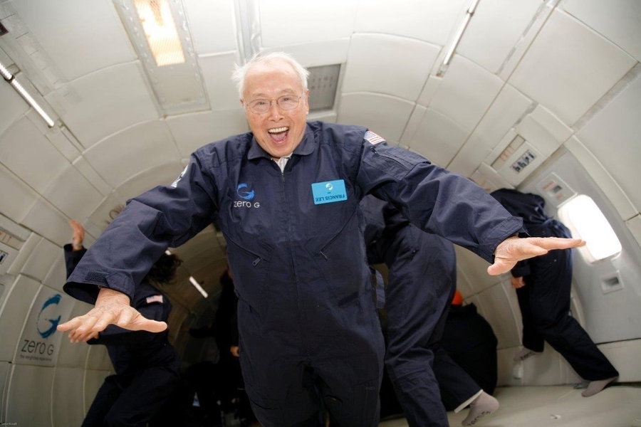 An elderly Francis Fan Lee wears a blue jumpsuit and an expression of pure joy while floating mid-air on a reduced-gravity aircraft.