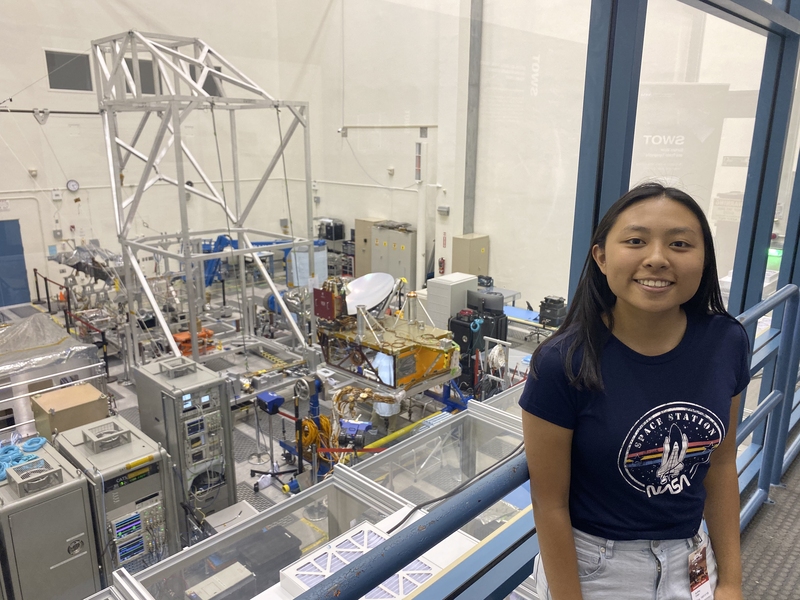 Audrey Chen wearing a NASA T-shirt smiles on a catwalk over a room full of machinery