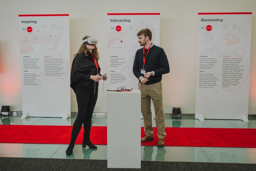 Two people wearing lanyards stand on a stage, one of them in a virtual reality headset