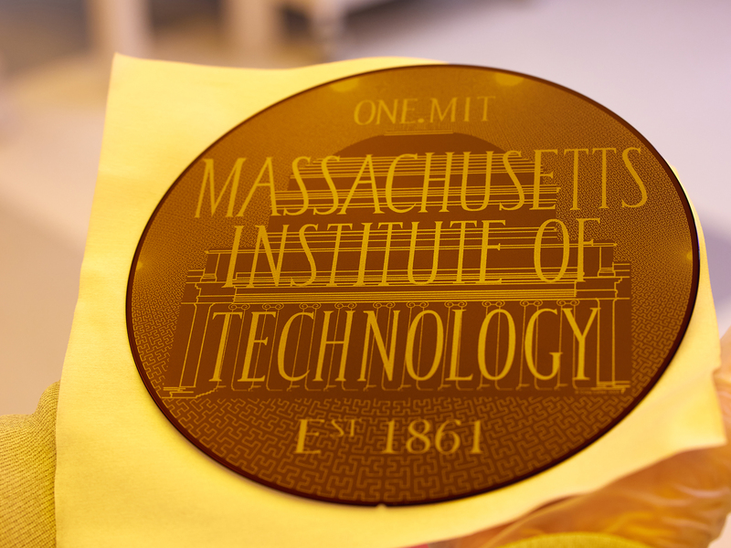 Hands holding a circular silicon wafer etched with "Massachusetts Institute of Technology Est. 1861"