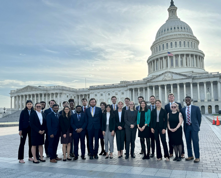 24 people in business attire pose in a line in front of the U.S. Capitol