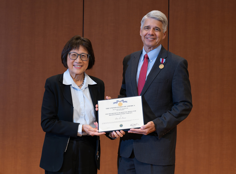 Heidi Shyu and Eric Evans stand side-by-side holding up a plaque between them. Evans has a medal pinned to his lapel.