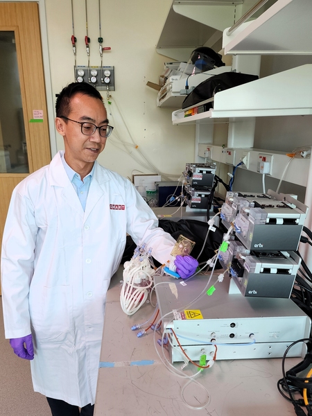 Wei-Xiang Sin, in lab coat and nitrile gloves, examines a cassette-sized object over a lab bench