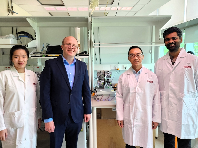 Denise Teo, Michael Birnbaum, Wei-Xiang Sin, and Narendra Suhas Jagannathan flank their microbioreactor system, about the size of a small printer