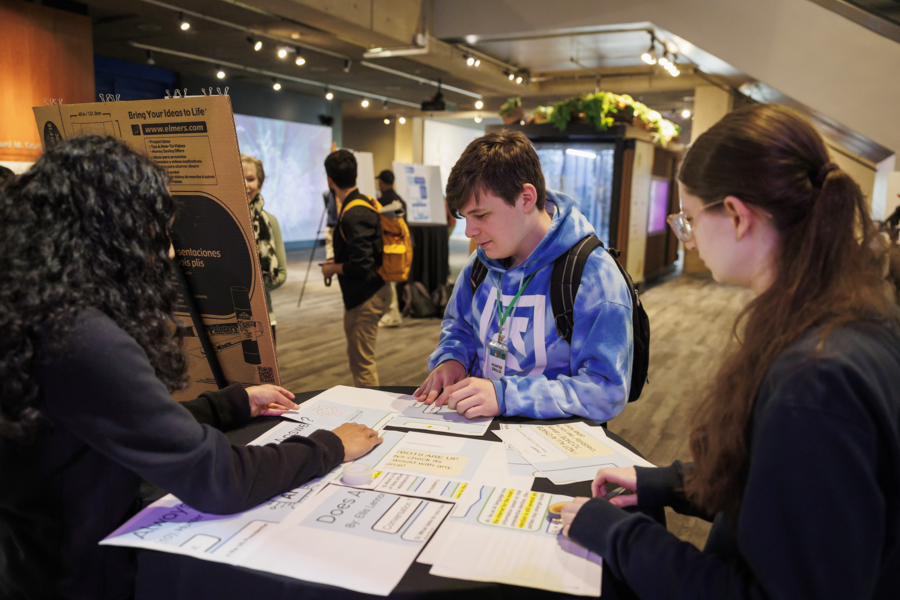 Three students look at a papers on a table. 