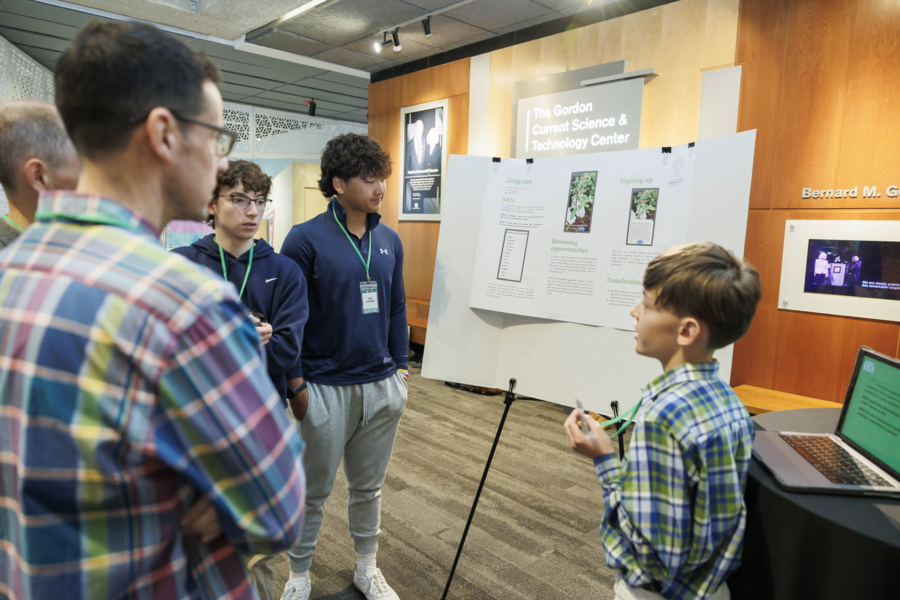 Four students stand around a scientific poster.