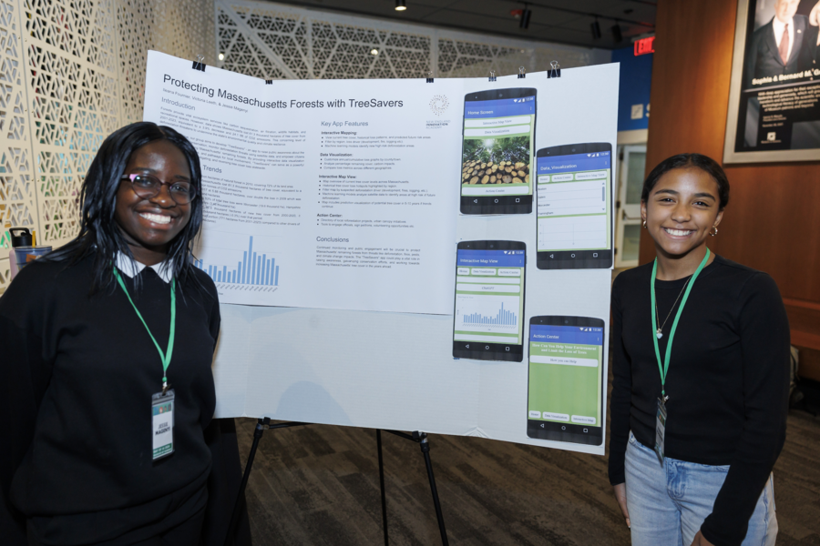 Two students smile while flanking their poster. 