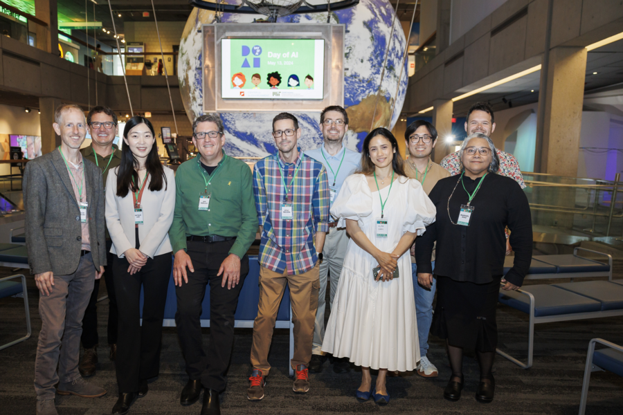 Ten people pose, smiling, with a screen behind them displaying a Day of AI slide.