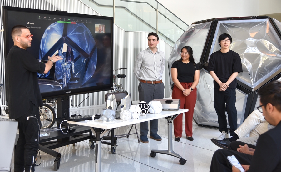 Four people at a presentation with a prototype on a table and a screen behind it.