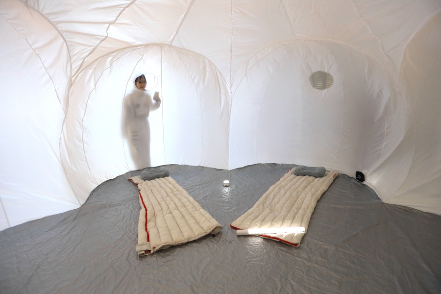 A woman looks through a porthole into an inflatable tent with two sleeping bags on the floor