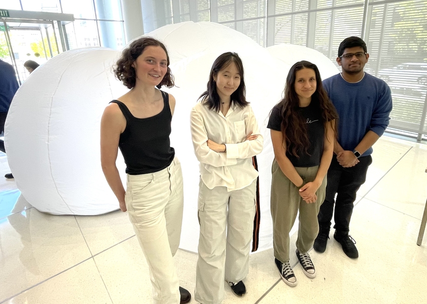 Four people stand in front of a white tent comprised of three inflated spheres.