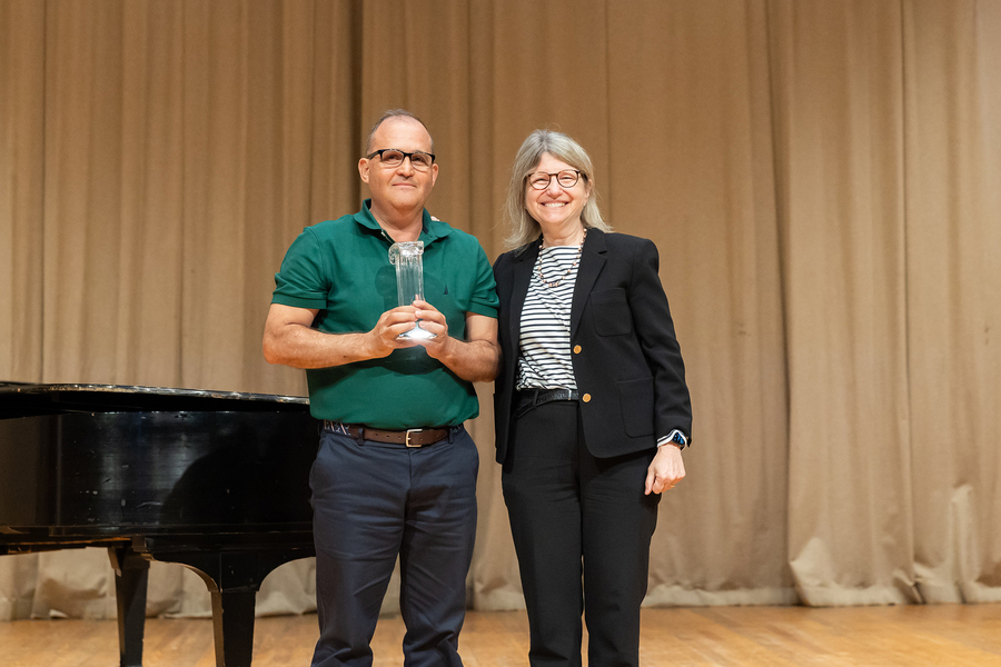 A man wearing a polo shirt is holding an award and standing next to a woman who is smiling and wearing a black suit.