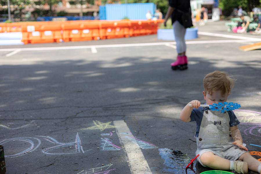 A young child plays with bubbles, with outdoor roller rink in the background.