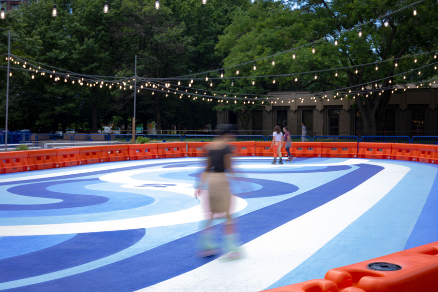 An out-of-focus roller skater skates at an outdoor rink.