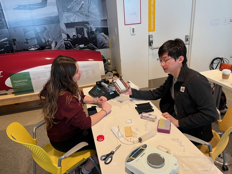 Rachael Rosco and Brandon Sun face one another across a desk strewn with various tools and components