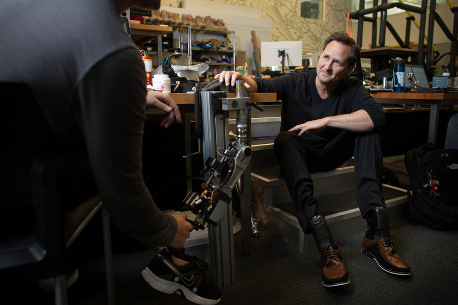 Hugh Herr, who wears two prosthetic legs, speaks to someone holding a prosthetic leg.