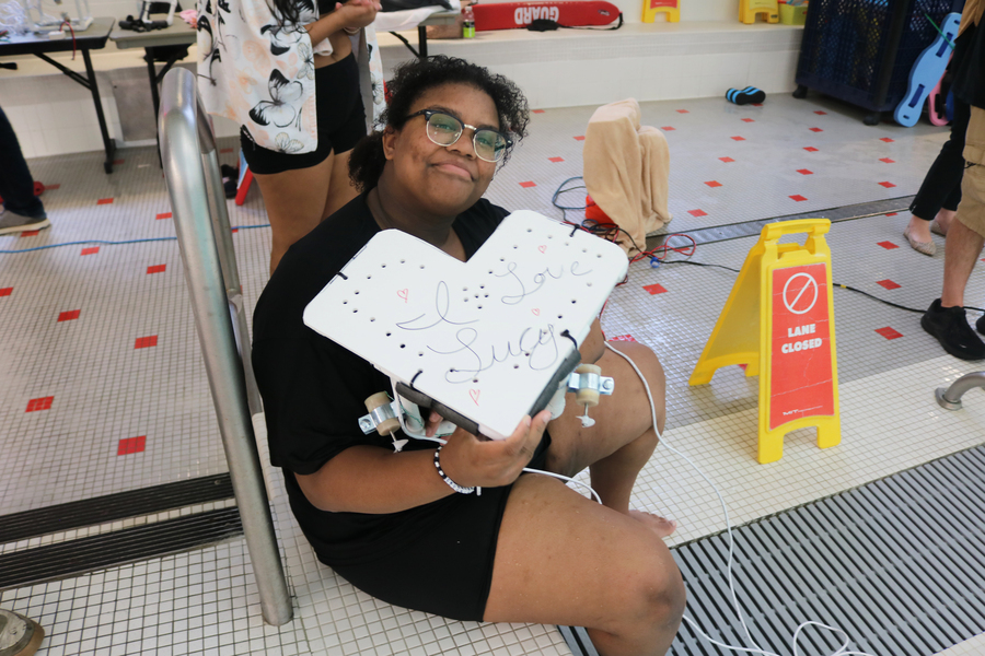 Student sitting by the pool holds a heart-shaped ROV that reads “I love Lucy”