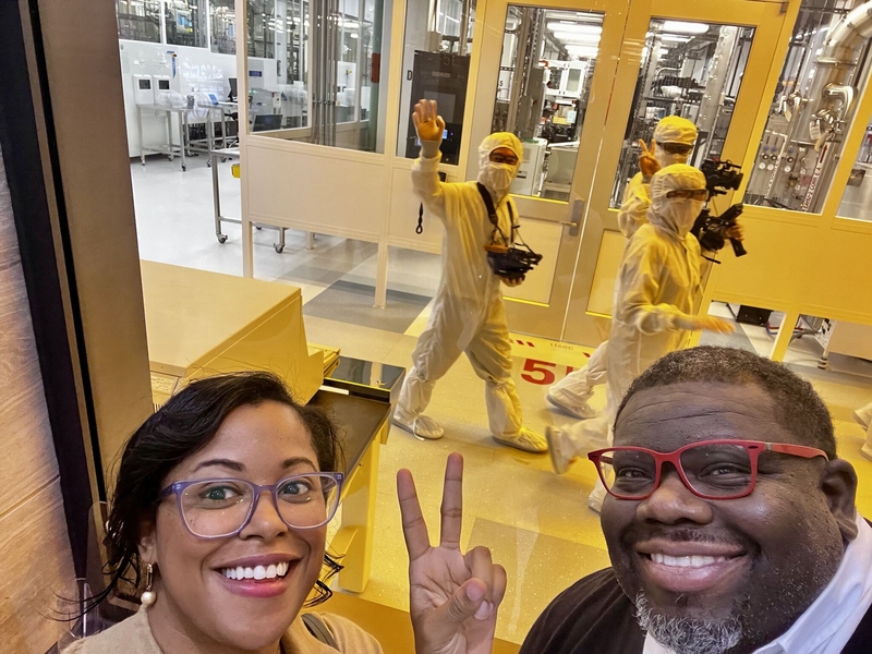 Chelsee Young and Quincy Moore III take a selfie before three people in bunny suits walk through an MIT.nano cleanroom